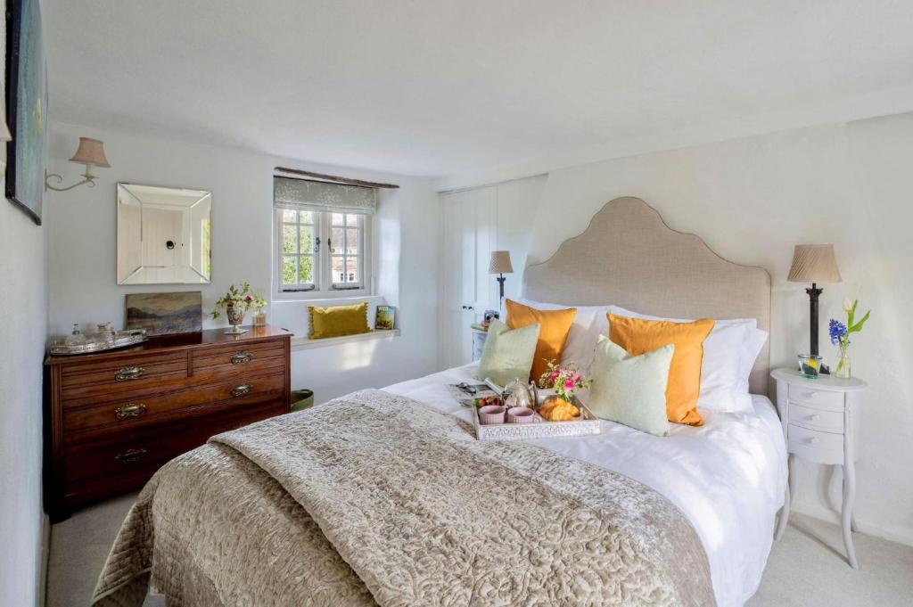 a white bedroom with a large bed with orange pillows at Tudor Rose Cottage in Stourpaine