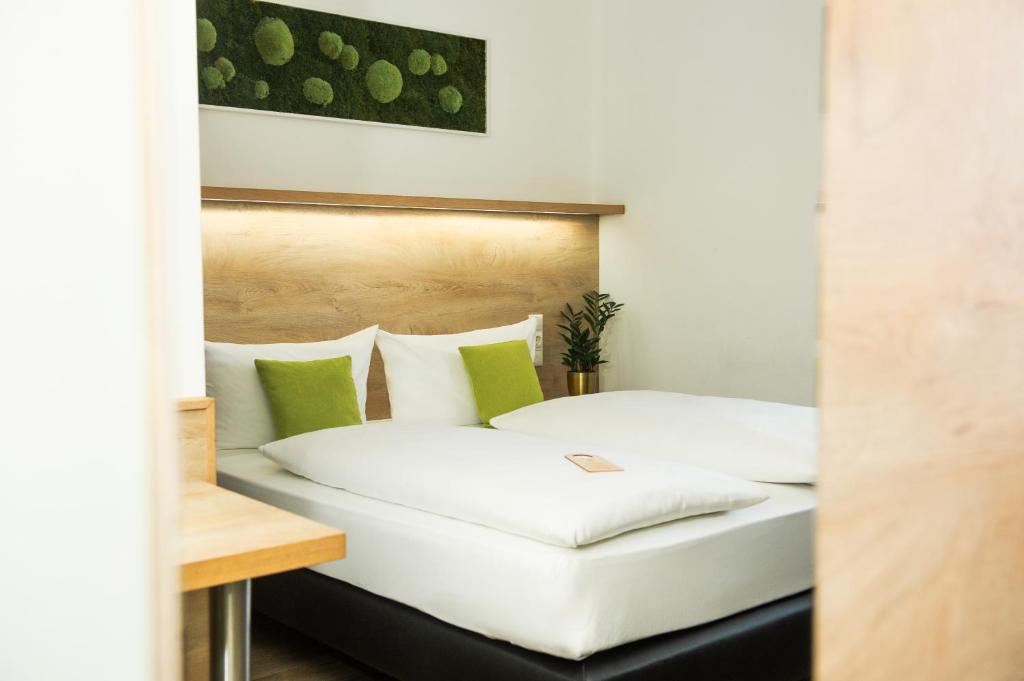 a bedroom with two white beds with green pillows at Hotel Perlach Allee by Blattl in Munich