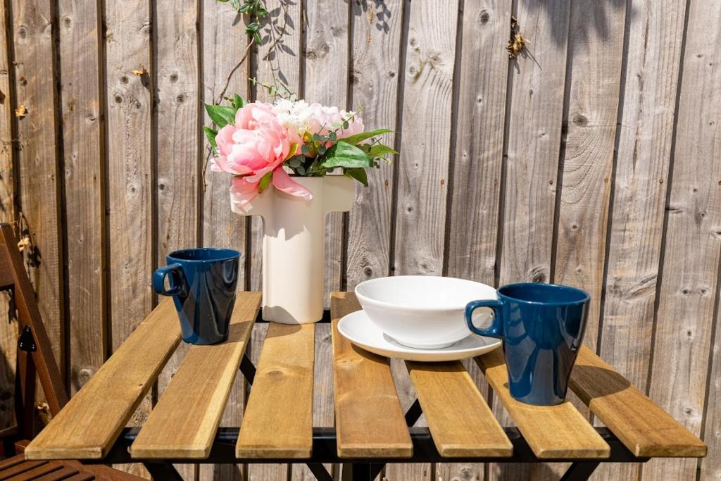 a table with a vase of flowers and two cups at Rooms Close to Canary Wharf in London