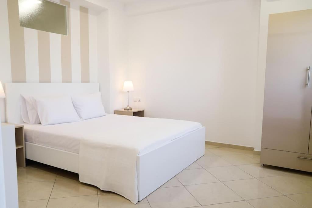 a white bed in a white room with a lamp at Cozy apartment near Airport in Koropi