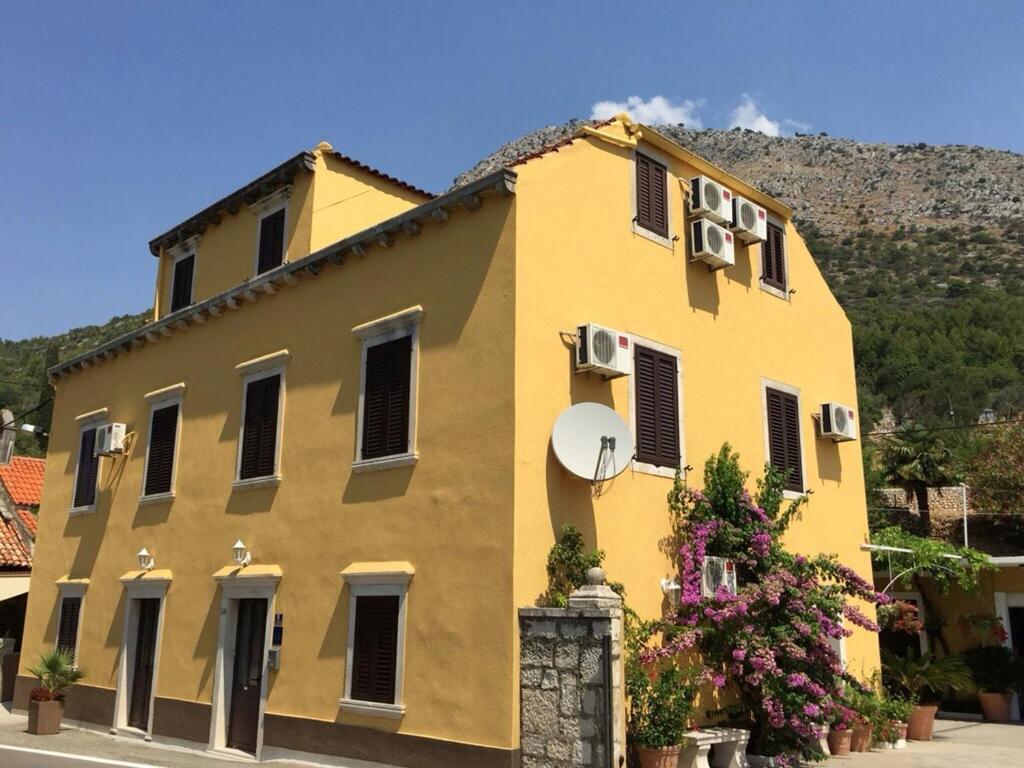 un edificio giallo con una montagna sullo sfondo di Rooms Mozara a Trsteno