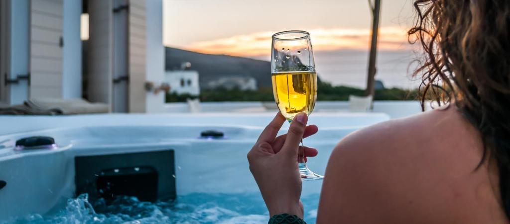a woman holding a glass of wine in front of a tub at Milia Gi Suites in Pollonia