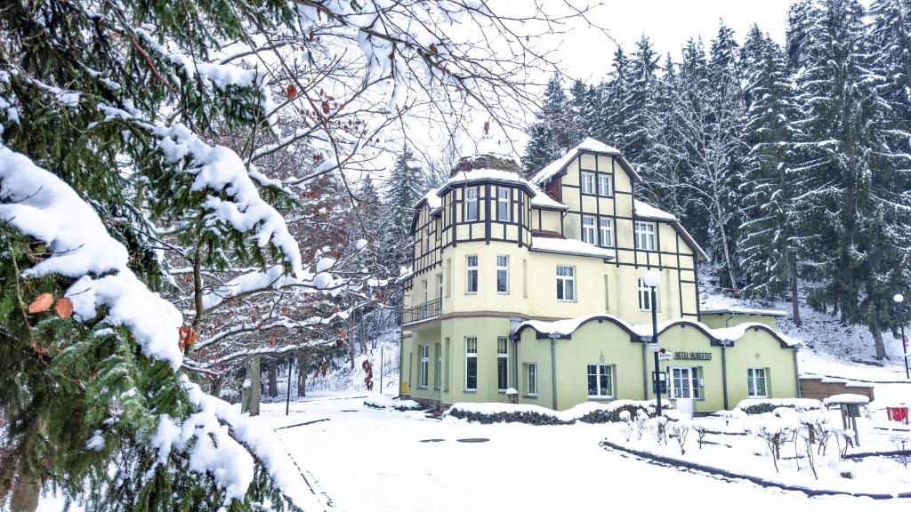 uma grande casa amarela na neve com árvores em Hotel Hubertus em Karlovy Vary