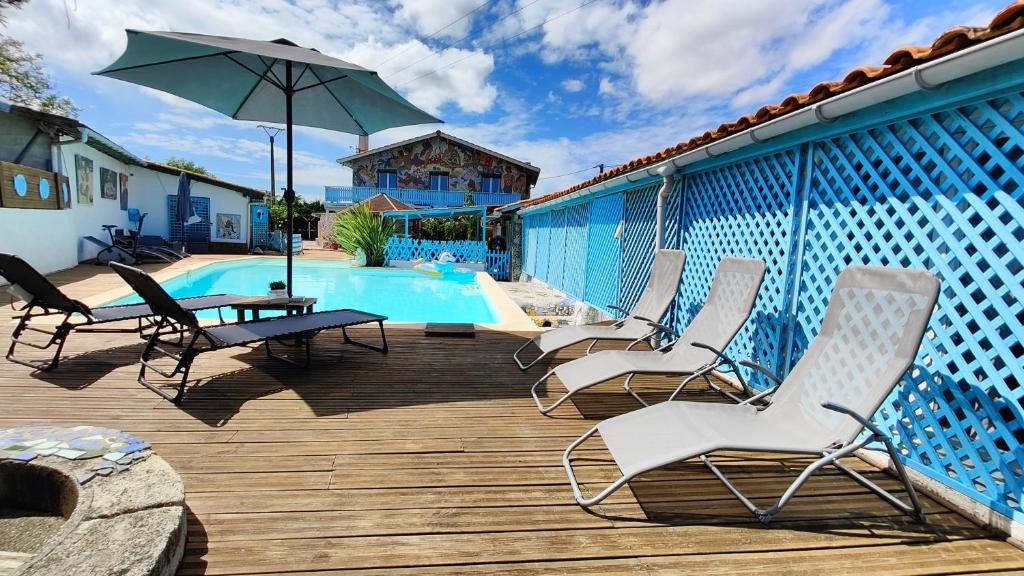 eine Terrasse mit Stühlen und einem Sonnenschirm neben einem Pool in der Unterkunft La Maison Mosaic Medoc - Gîtes in Gaillan-en-Médoc