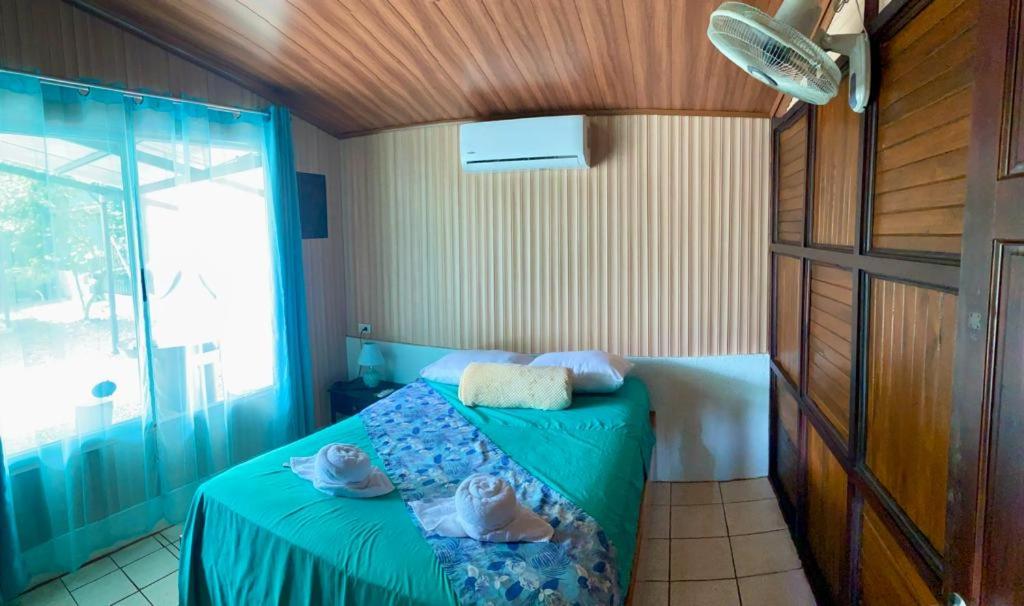 a bedroom with a bed with a green blanket and a window at Cabaña que Tuanis in Fortuna