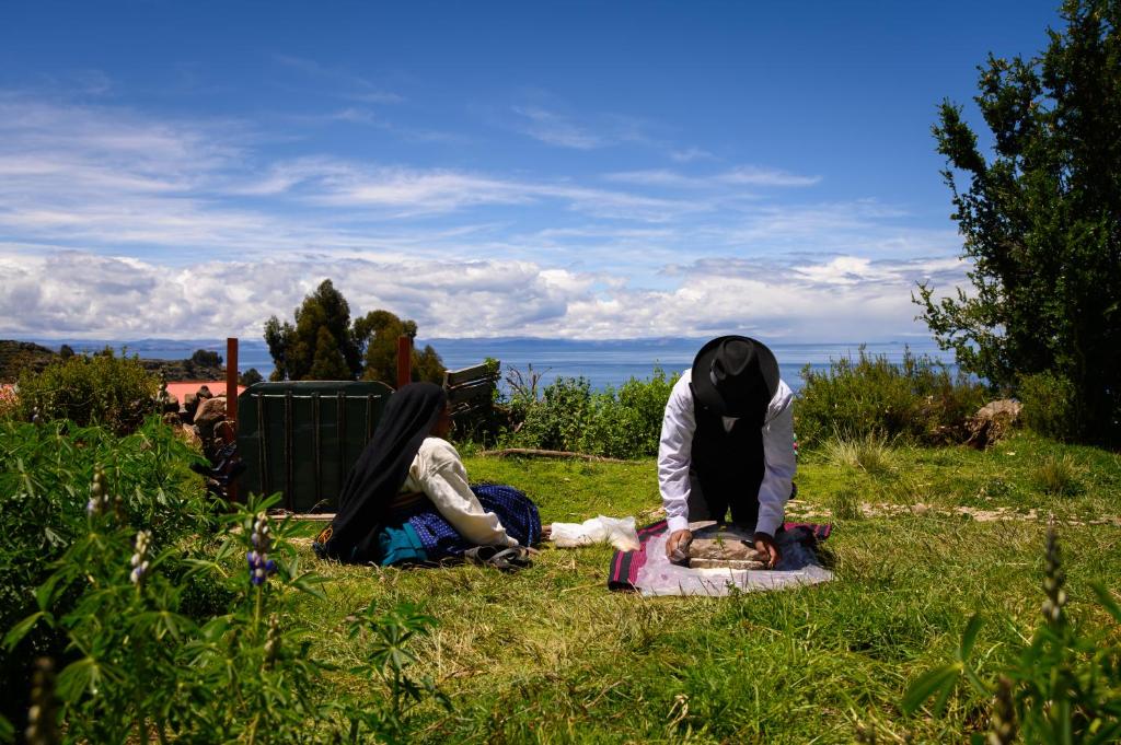 two people sitting on the grass in the grass at Quinuawasi House in Ocosuyo