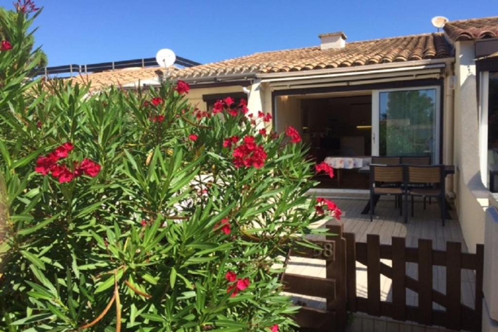 une maison avec une brousse et des fleurs rouges dans l'établissement Naturiste Cap d'Agde Villa Héliovillage 58, au Cap d'Agde