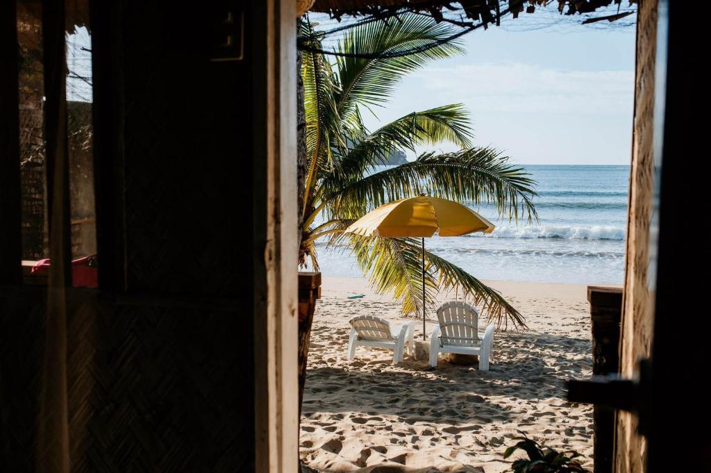 een uitzicht op een strand met 2 stoelen en een parasol bij Bucana Beach Camp in El Nido