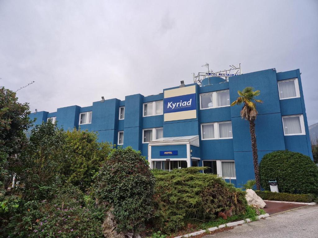 a blue hotel with a palm tree in front of it at Kyriad Toulon Est Hyeres La Garde in La Garde