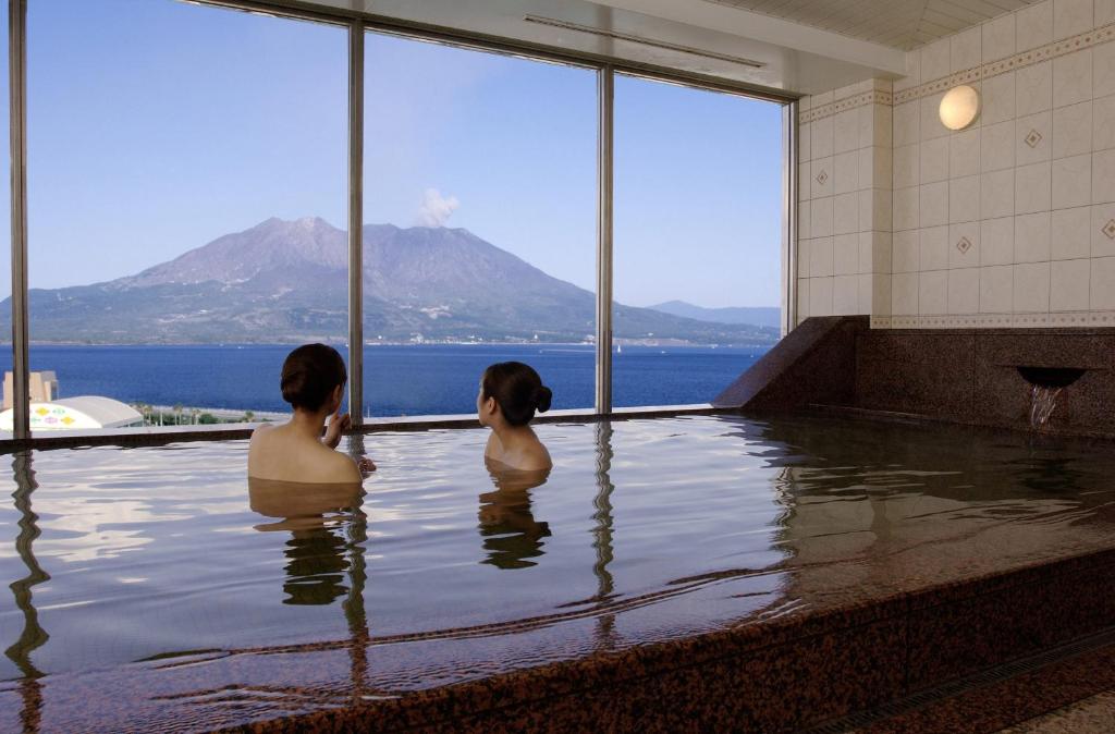 duas mulheres sentadas numa piscina com vista para a água em Kagoshima Sun Royal Hotel em Kagoshima
