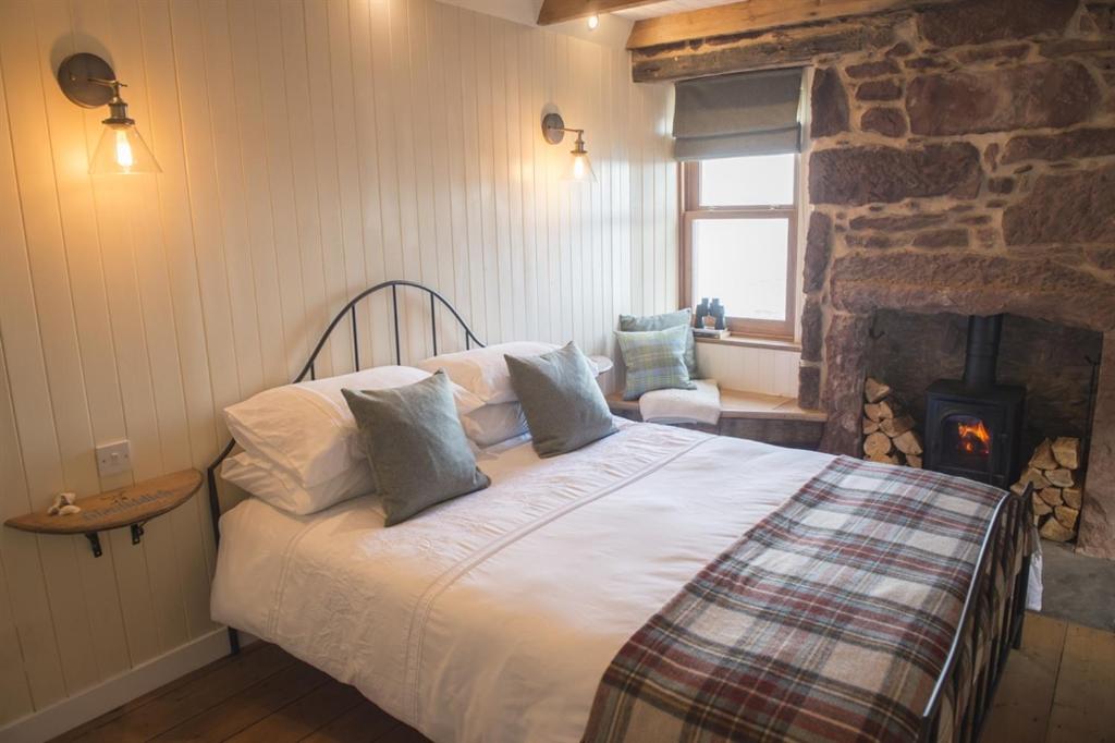 The Wee House في Pennan: غرفة نوم مع سرير ومدفأة حجرية