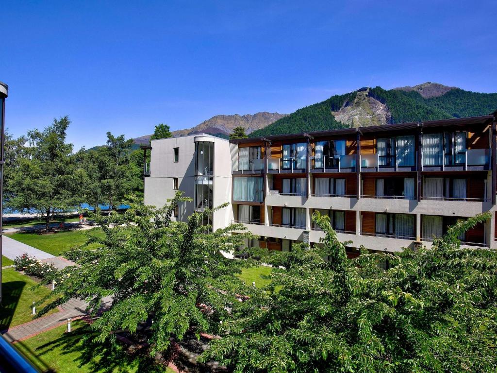 a building with trees in front of a mountain at Novotel Queenstown Lakeside in Queenstown