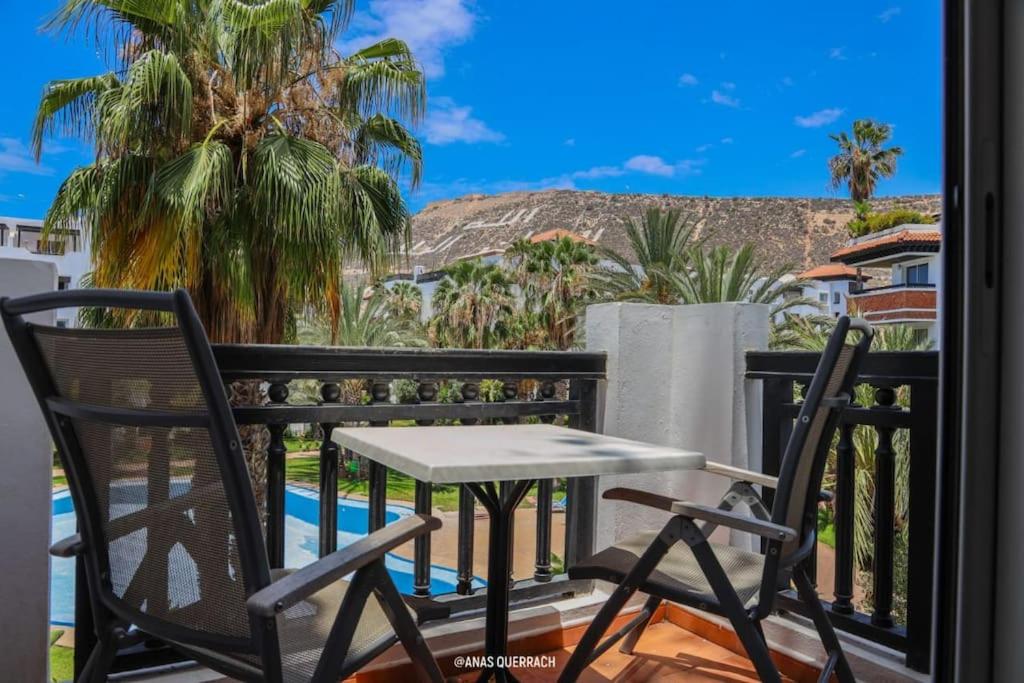 a table and chairs on a balcony with palm trees at Appartement vue piscine à marina in Agadir