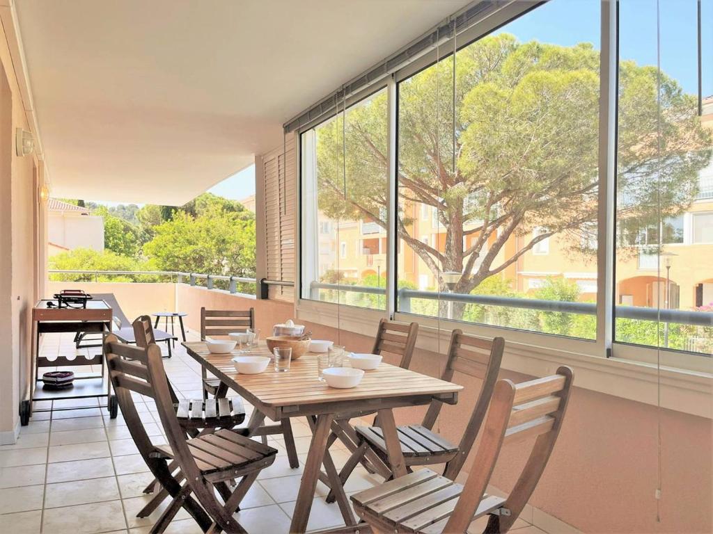 une salle à manger avec une table, des chaises et des fenêtres dans l'établissement Appartement climatisé avec piscine, terrasse et parking - 6 couchages, près de la plage - FR-1-251-451, au Lavandou