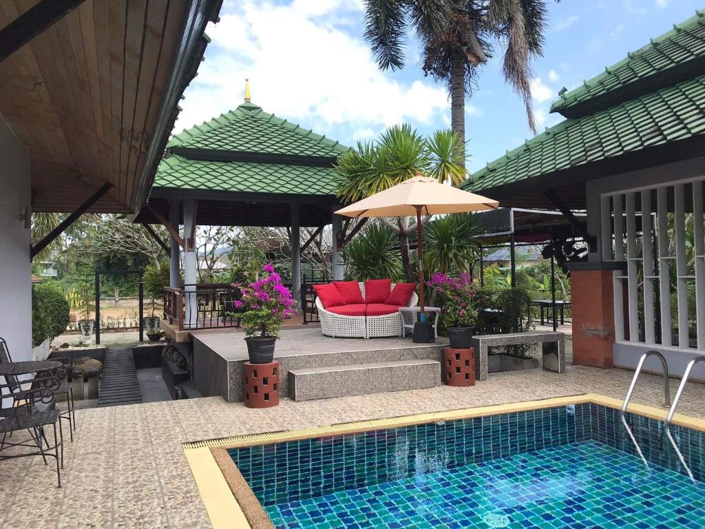 a swimming pool with a red chair and an umbrella at Plumeria Villa Thalang in Ban Pak Lak