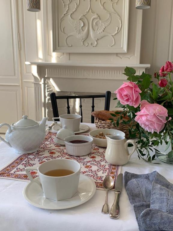 une table avec des tasses et des soucoupes sur une table avec des roses dans l'établissement Chambre Suite d'hôte à Ouville la Rivière Normandie, à Ouville-la-Rivière