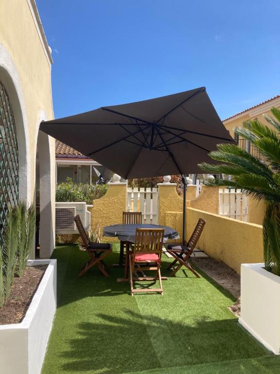 un patio avec une table, des chaises et un parasol dans l'établissement Village naturiste - Jardin de la Palmeraie - Villa 2 chambres -, au Cap d'Agde