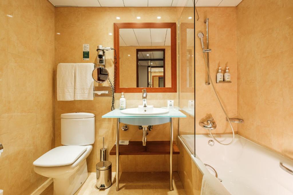 A compact bathroom places a toilet, glass-enclosed shower and bathtub around a central basin.