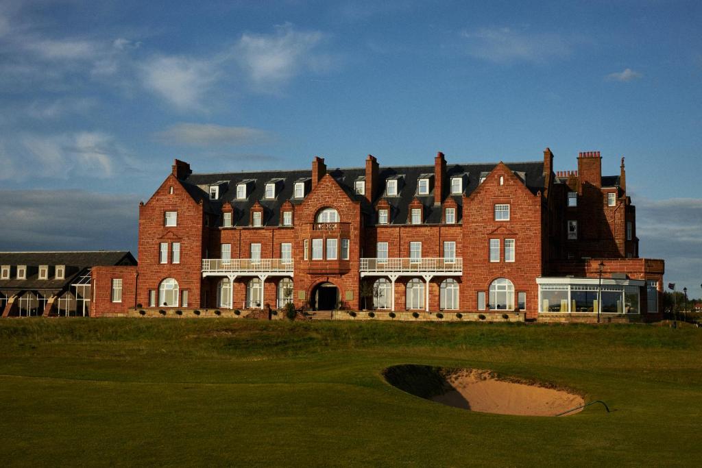 een groot gebouw van rode baksteen met een gat in het gras bij Marine Troon in Troon