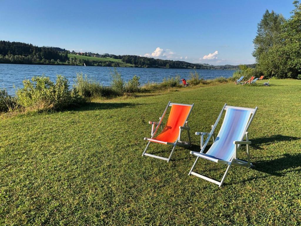 2 chaises longues assises sur l'herbe à côté d'un lac dans l'établissement Ferienwohnung Seeglück, 