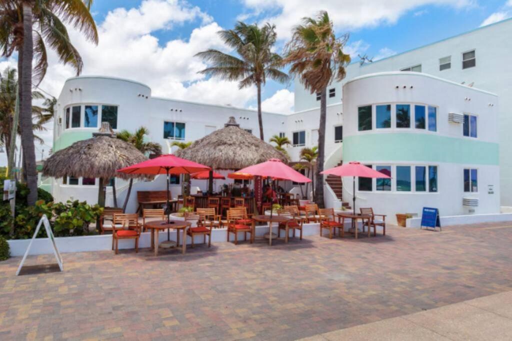 a group of tables and chairs with umbrellas in front of a building at Walkabout 3 King Suite on the Ocean in Hollywood Beach in Hollywood