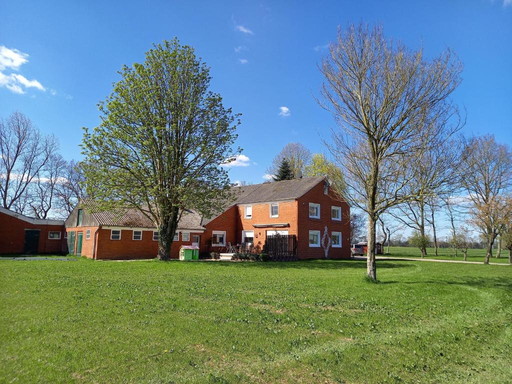 una grande casa rossa con un albero in un campo di Ferienhaus Dat Landhuus 95158 a Rhauderfehn