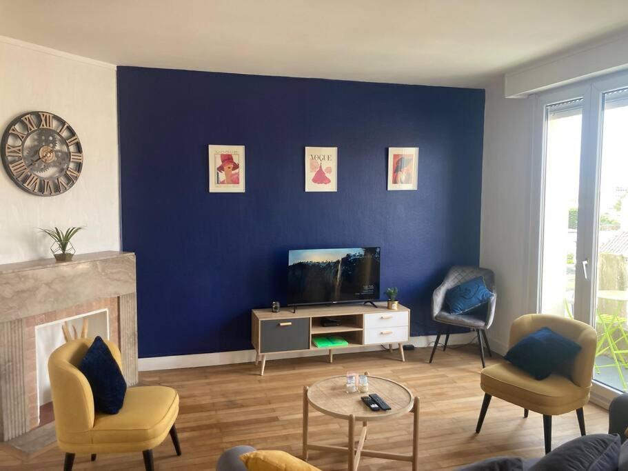 Il comprend un salon doté d'un mur bleu, d'une télévision et de chaises. dans l'établissement Appart tout confort à 100m de la plage de Malo., à Dunkerque