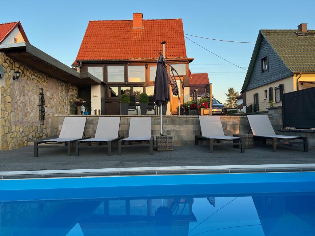 Una piscina con sillas y una sombrilla al lado de una casa. en Ferienhaus Eisfelder Blick, en Eisfeld