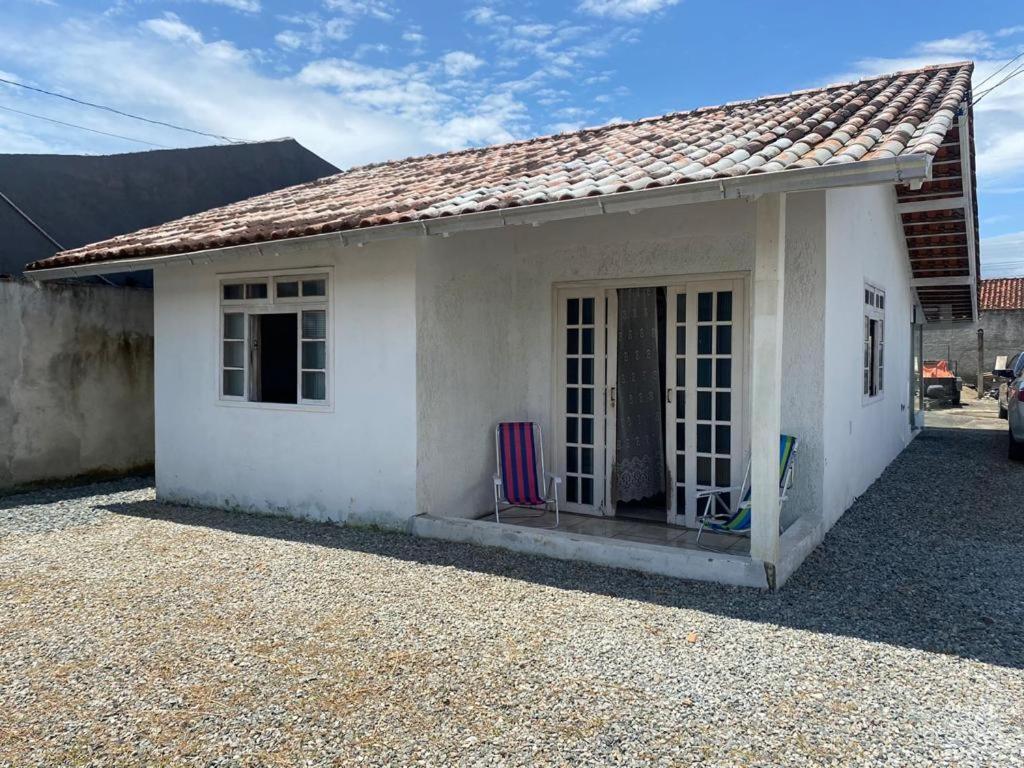 una pequeña casa blanca con una silla delante en Casa Praia NAVEGANTES GRAVATÁ en Navegantes