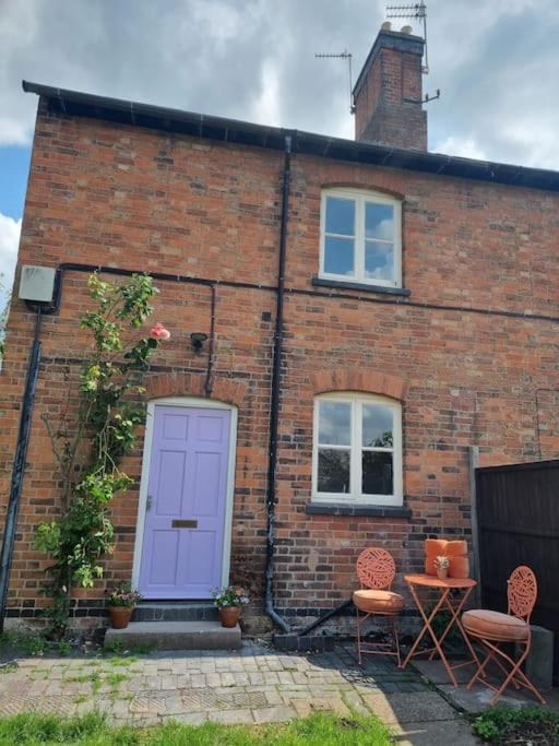 a brick house with a purple door and two chairs at 2 Bedroom Cosy Cottage in Rearsby