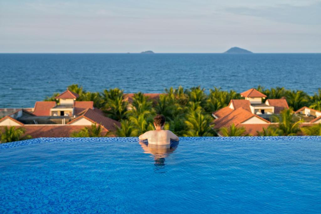 un hombre en una piscina mirando hacia el océano en Fivitel Hoi An Hotel, en Hoi An