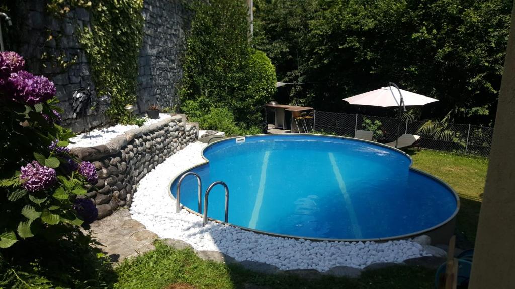 einen Pool in einem Garten mit einer Steinmauer und einem Sonnenschirm in der Unterkunft Sonnenschein in Brione sopra Minusio