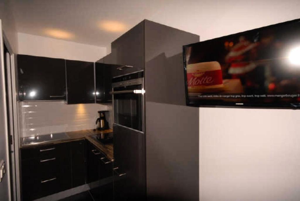 une cuisine avec des placards noirs et une télévision murale. dans l'établissement Résidence SANCTUS - Studio pour 6 Personnes MAE-9054, à Gourette