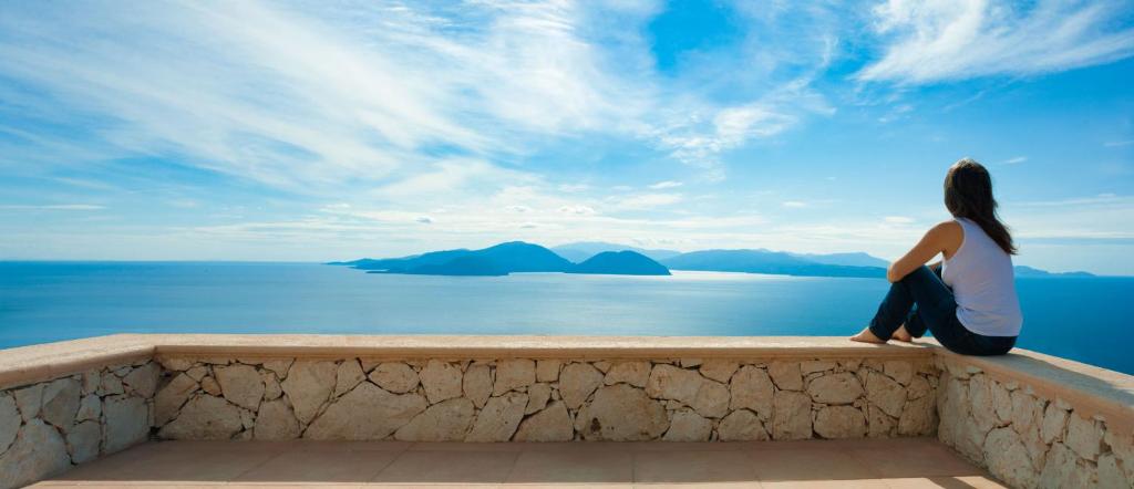 una mujer sentada en una cornisa mirando hacia el océano en Heliopetra Luxury Villa Lefkas, en Vasiliki