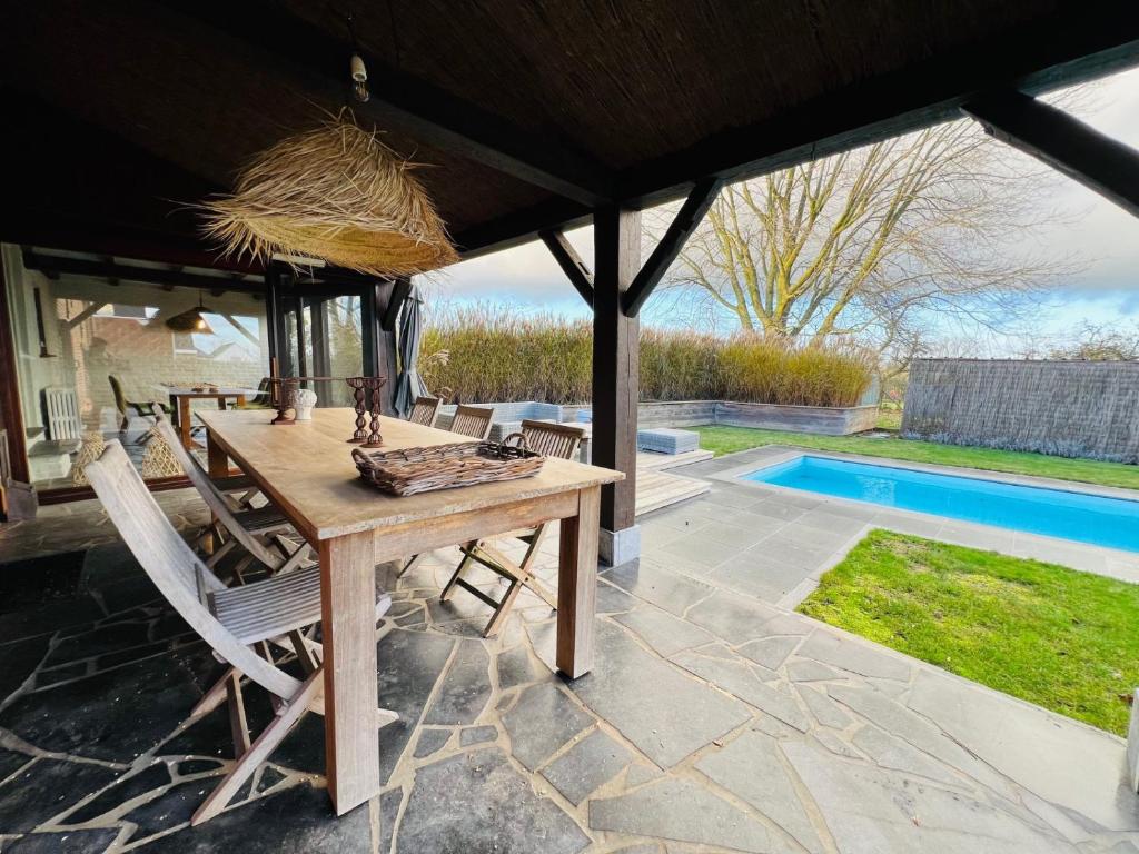 a wooden table and chairs under a pavilion with a pool at ZEN Op Vakantie @vakantiehoeve met zwembad in Lierde