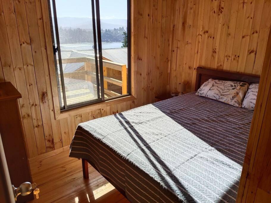 Cama en habitación de madera con ventana en Cabaña vista Lago Vichuquen, en Vichuquén