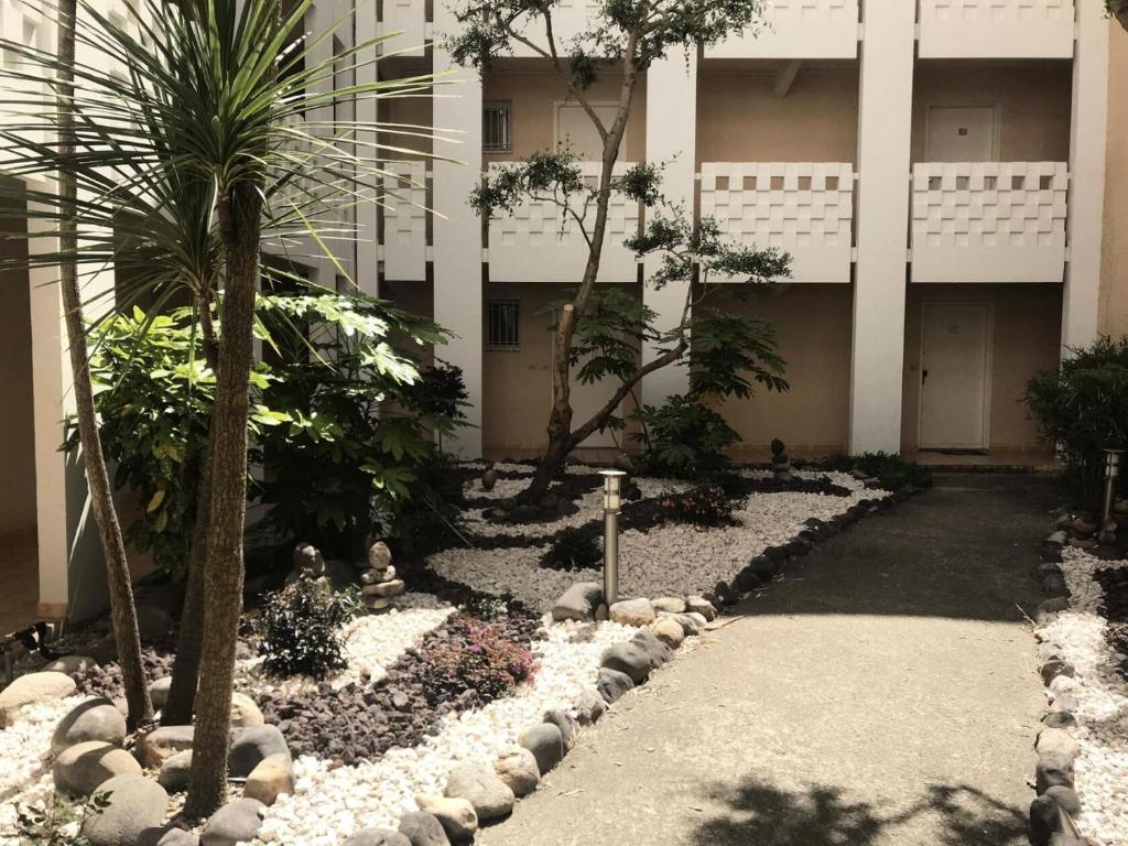 une cour d'un bâtiment avec des palmiers et des rochers dans l'établissement Résidence Grand Large - Charmant T3 proche plage dans un beau domaine avec piscine MAE-1214, à Six-Fours-les-Plages