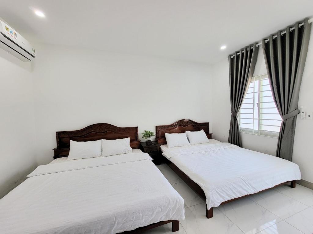 2 camas en una habitación con paredes blancas y ventana en Amy Motel Xuyên Mộc en Xuyên Mộc