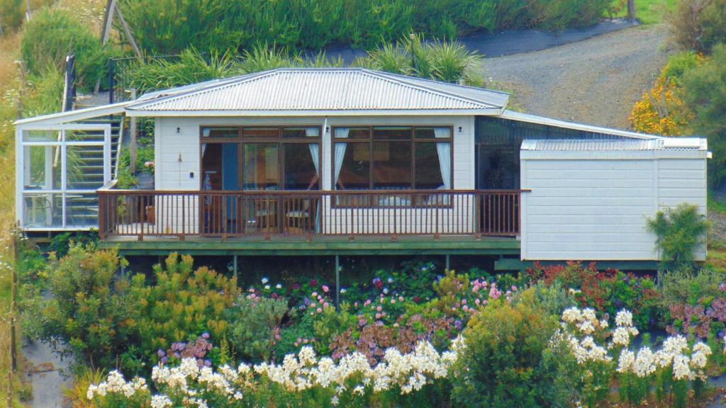a house with a deck in a garden with flowers at Raglan's Tranquil Garden Retreat - Moa Stone Lodge in Raglan