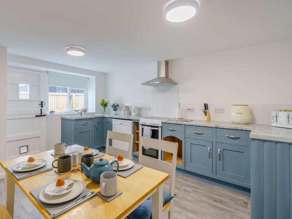 een keuken met blauwe kasten en een tafel en stoelen bij 2 Bed in Cockermouth 85680 in Bridekirk