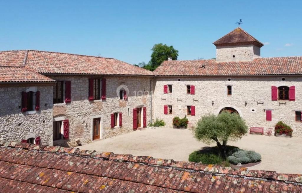 um antigo edifício de pedra com janelas vermelhas e uma árvore em Château de Famille em Créon-dʼArmagnac