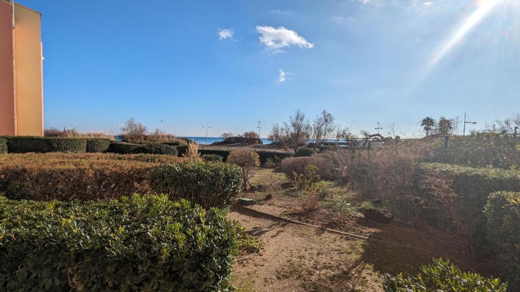un jardin avec des buissons, un bâtiment et l'océan dans l'établissement 050 Plein sud - Bel appartement rez de chaussée avec pk et wifi, au Cap d'Agde