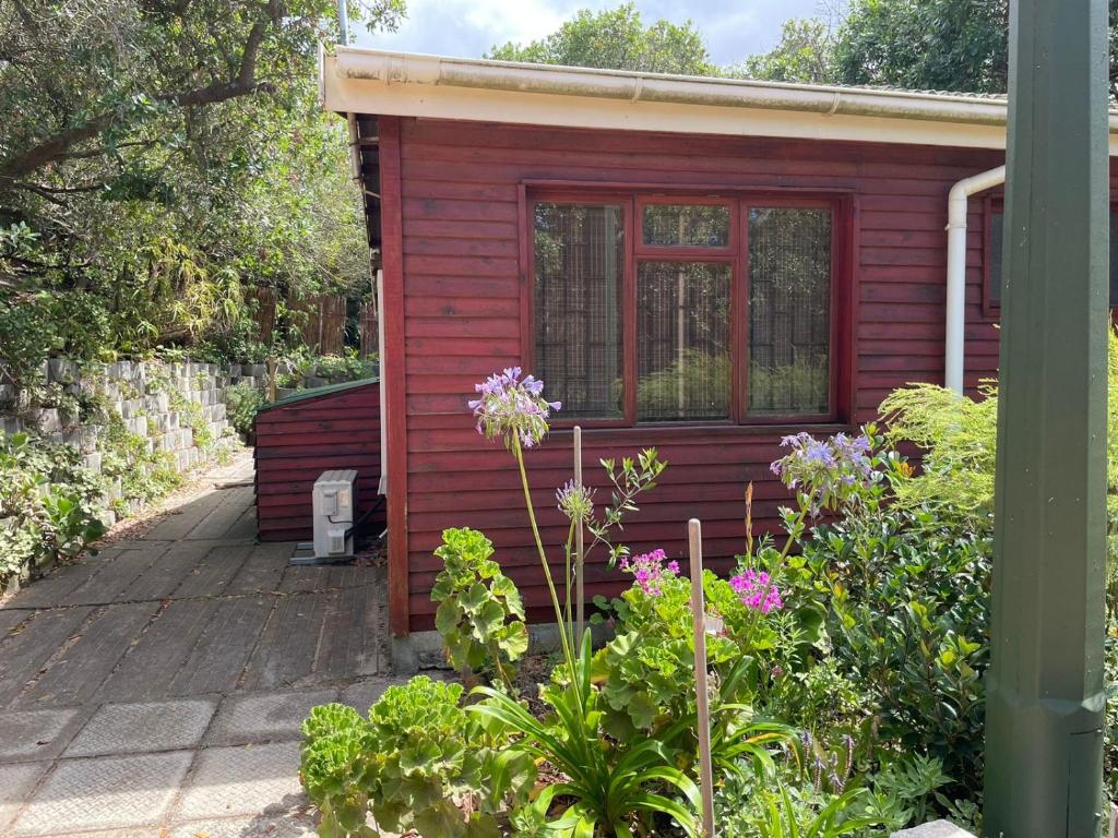 a red tiny house with a porch and some flowers at Peace and Rest in Hermanus