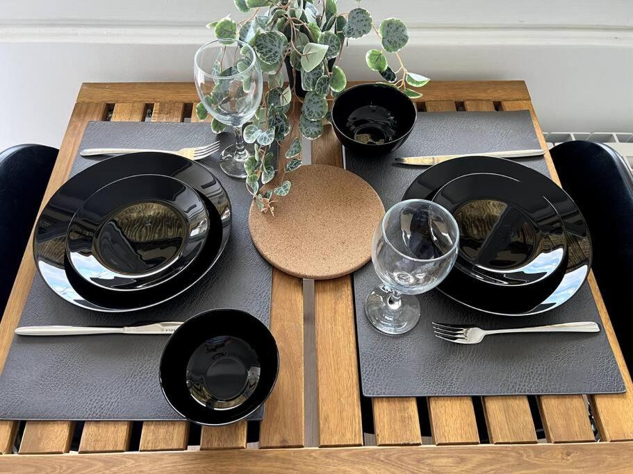 a wooden table with black plates and wine glasses at Studio cozy proche Paris in Gentilly