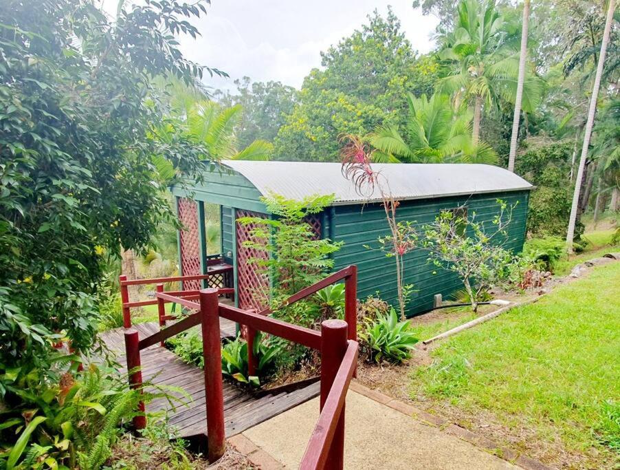 a small green house with a wooden bridge in front of it at Birdsong Train Carriage Cabin with Outdoor Bath in Palmwoods