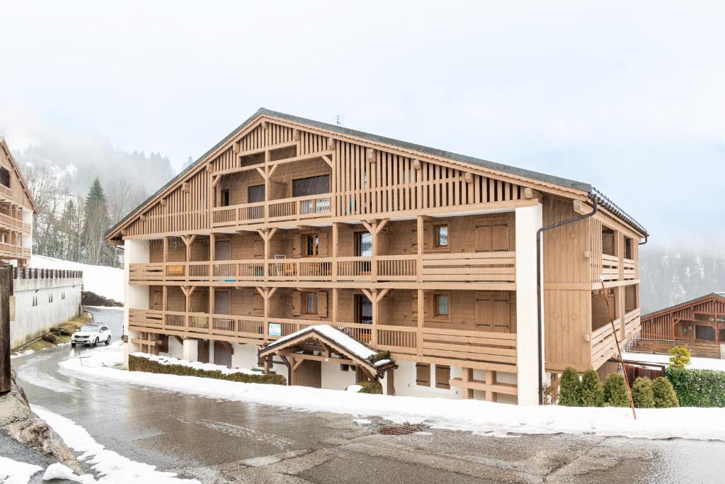 un grand bâtiment en bois avec de la neige au sol dans l'établissement Le Chemin des Alpages - Vue montagne, à La Giettaz