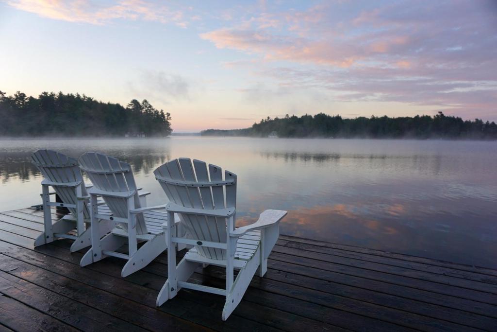 MinettにあるCozy Muskoka 4-bedroom cottage on Lake Rosseauの水辺の桟橋に座る白い椅子3脚