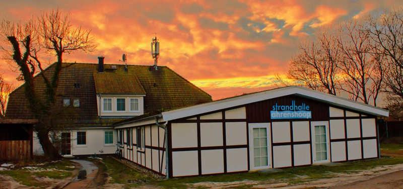 a building with a house with a sunset in the background at Gaestehaus _ Strandhalle in Ahrenshoop
