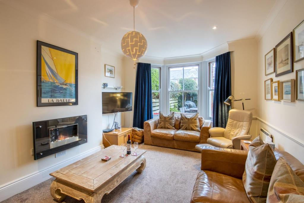 Living room with leather sofas, wooden coffee table, wall-mounted electric fireplace, and large bay window with dark curtains