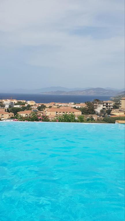 une grande piscine d'eau bleue avec une ville en arrière-plan dans l'établissement resd. cala di mare, à LʼÎle-Rousse